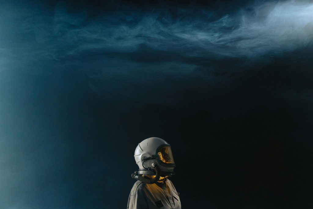 pexels-photo-7169857-7169857 Astronaut in a helmet looks toward the stars in a mysterious space setting.